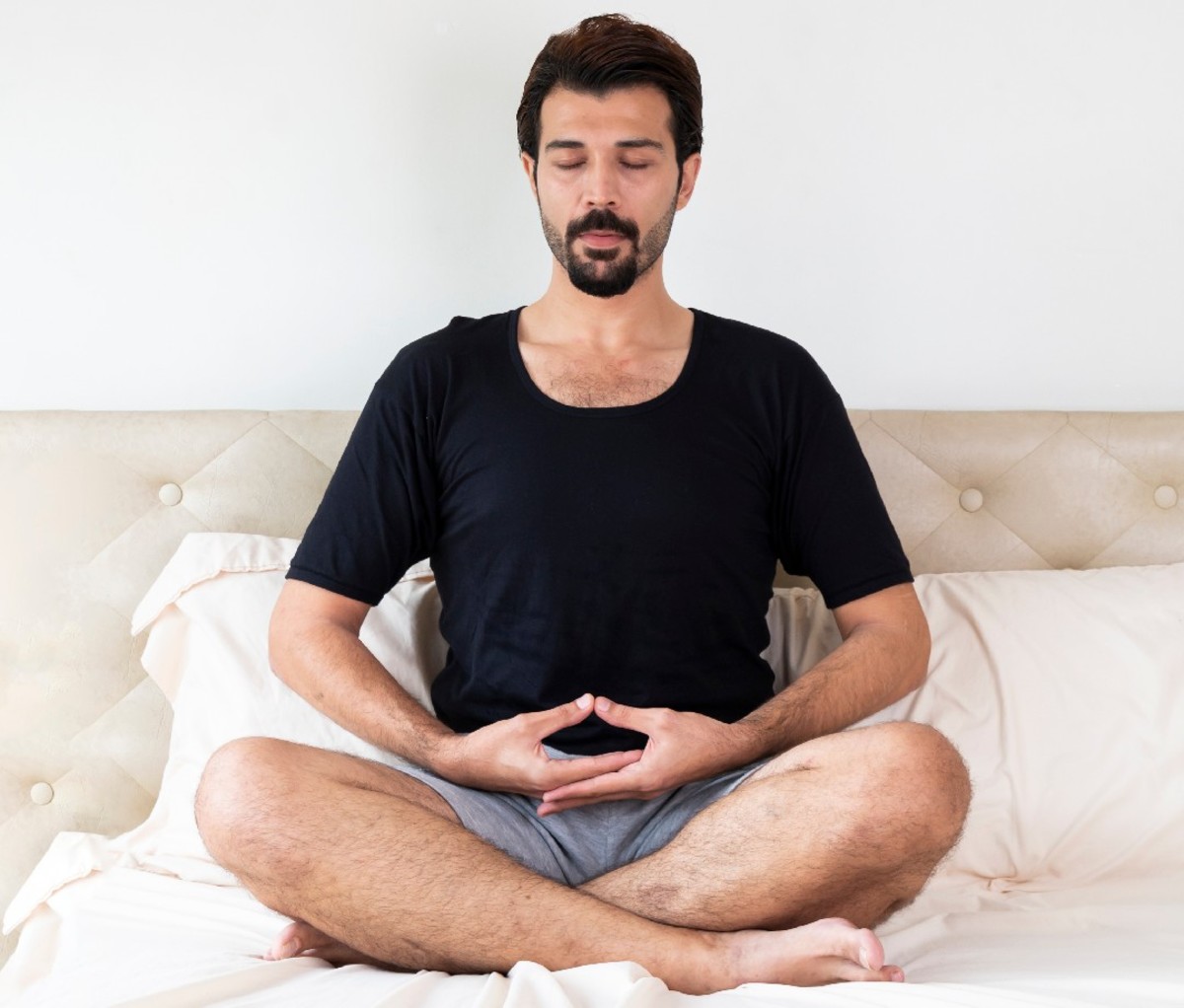 Man sitting cross legged on bed doing breathing exercise