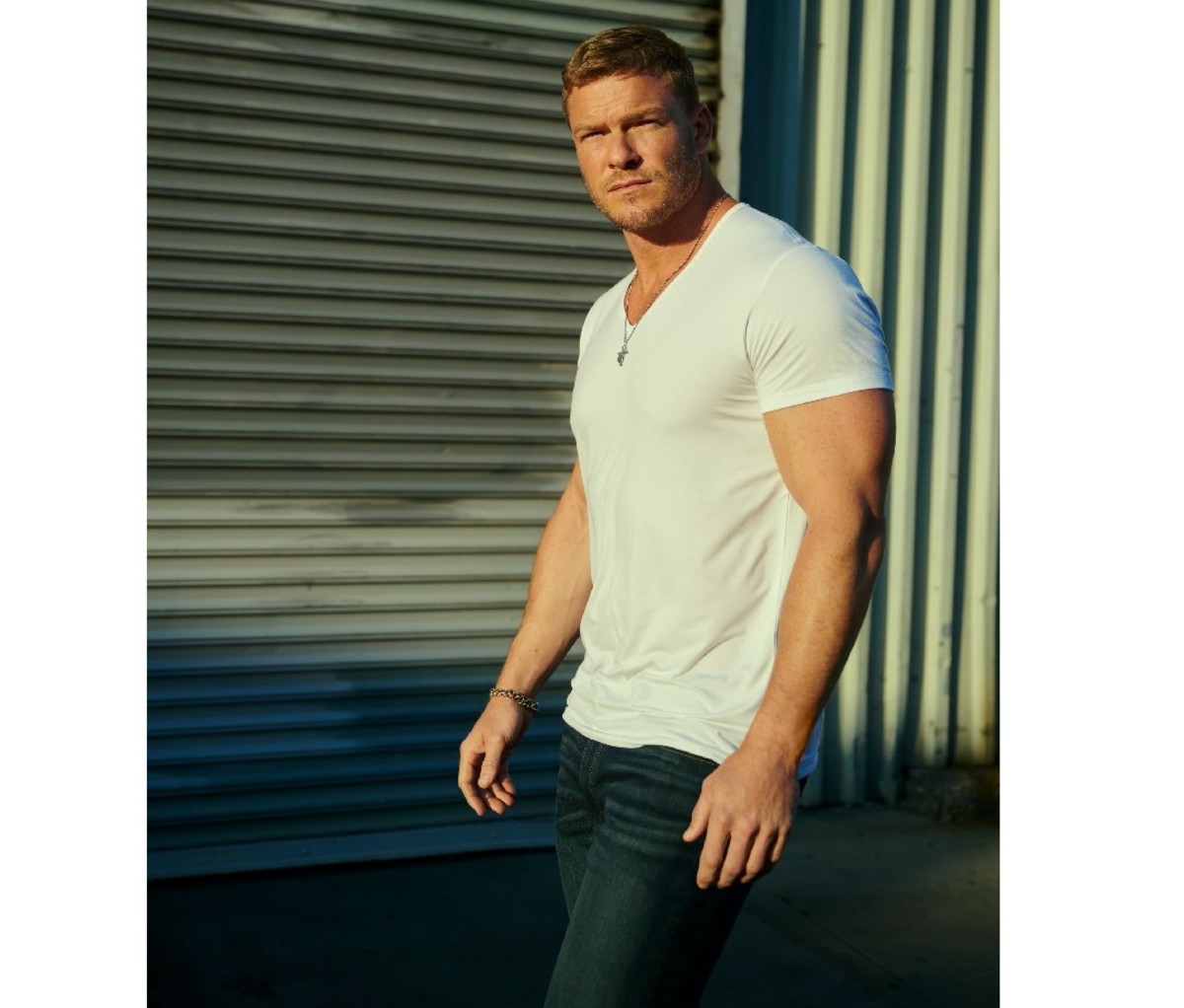 Actor Alan Ritchson stands outside in a white t-shirt during a scene from Amazon 