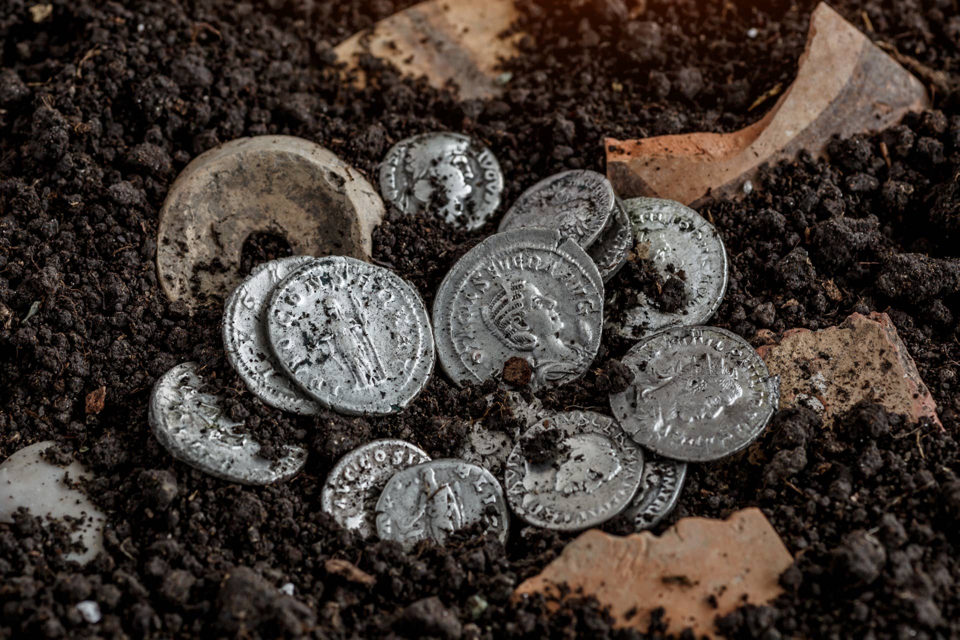 A pile of ancient, dirt-covered silver coins unearthed from the ground.
