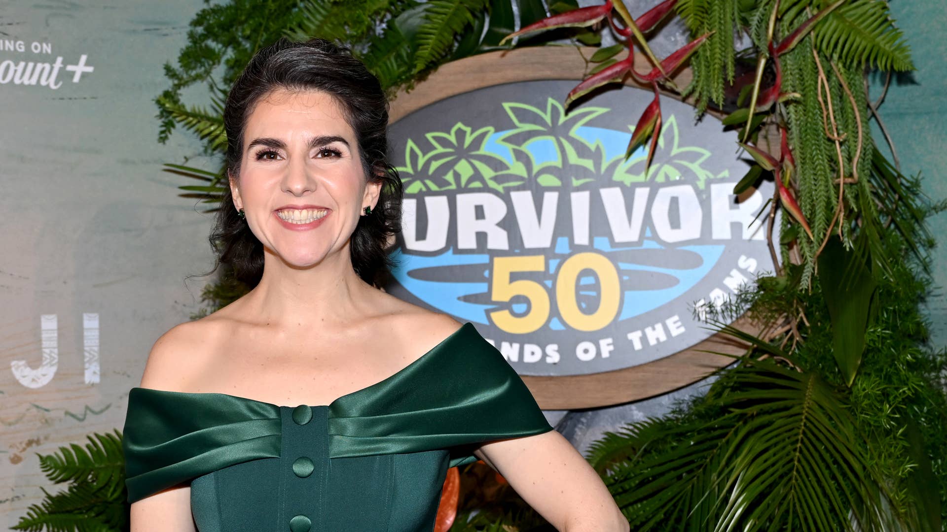 Aubry Bracco smiling on the red carpet next to the Survivor 50 logo.