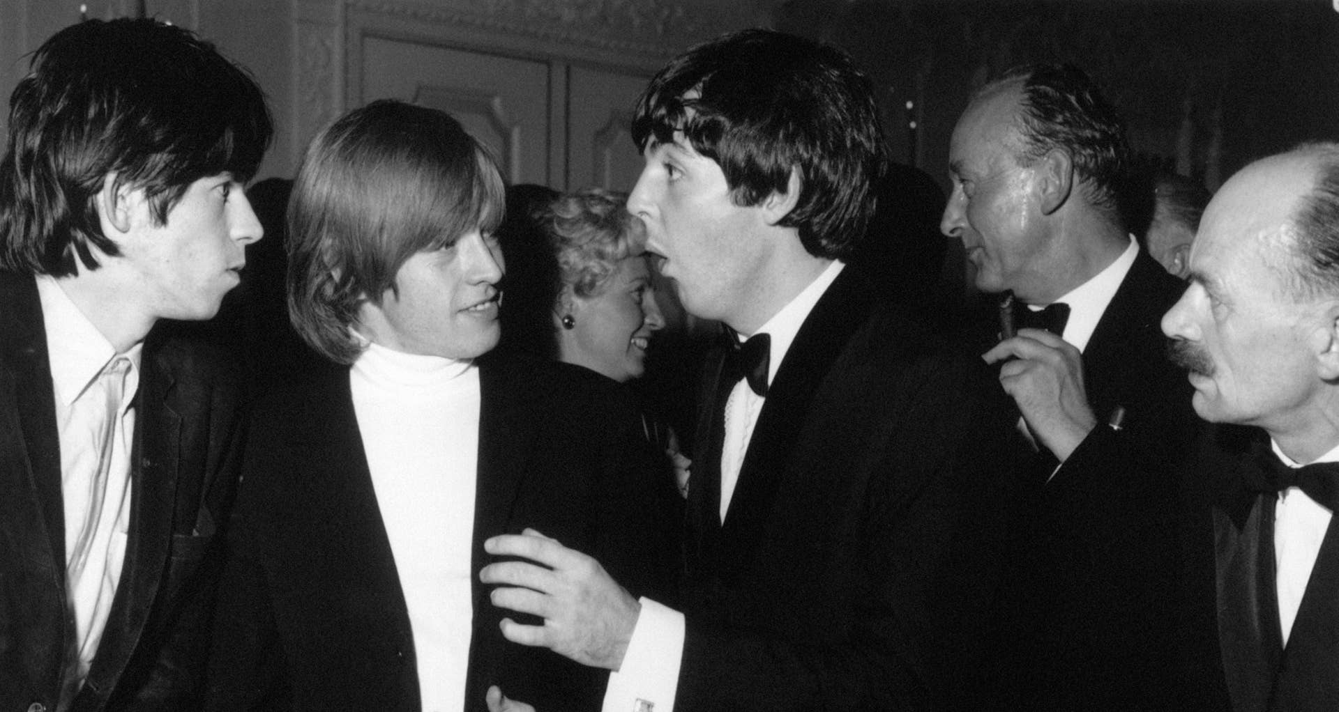 The Rolling Stones, Keith Richards (left) and Brian Jones, chat with Beatle Paul McCartney, in the early hours (7th July) at the Dorchester Hotel London, to celebrate the premiere (6th July) of The Beatles first film, A Hard Day’s Night, The Stones were celebrating too, their disc, It’s All Over Now, is top of the charts, pictured 2am Tuesday 7th July 1964.
