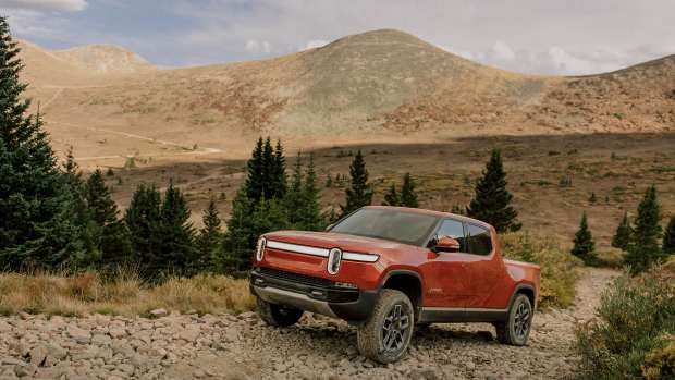Red Rivian R1T going up rocky path in mountainous area.