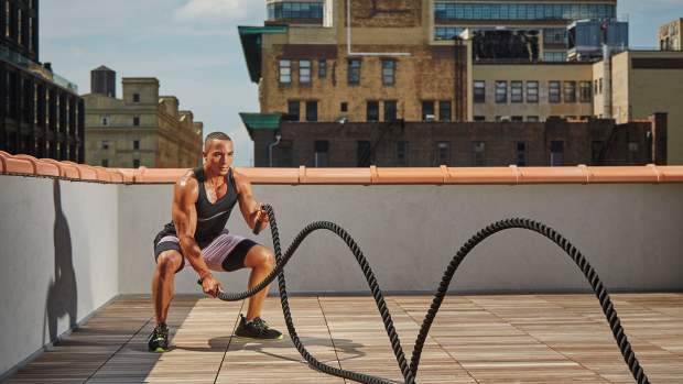 Black athletic man on urban rooftop doing battle rope waves, among the best love handle exercises