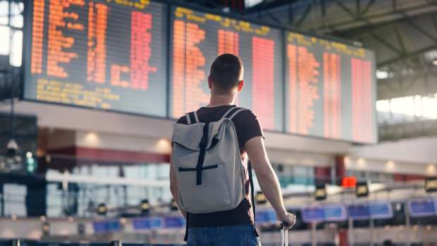 Stock photo of a man walking with backpack and suitcase walking through airport terminal and looking at departure information.