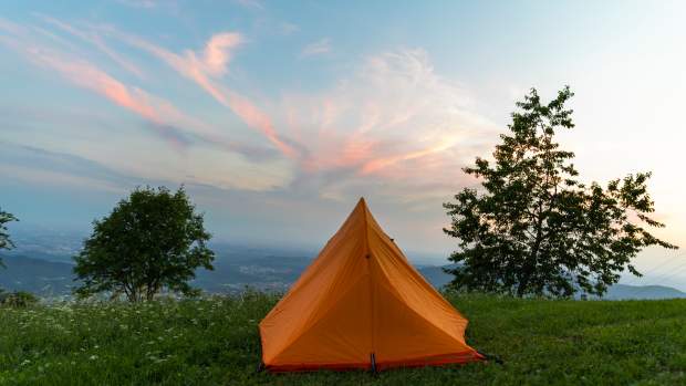 Camping tent in a meadow at the top of a hill at sunset.