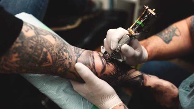 Stock photo of a tattoo artist tattooing a man's forearm.