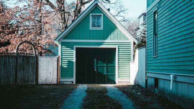 Green house and single car garage, painted green. At the end of a stone driveway.
