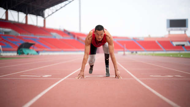 Amputee runner in red running with prosthetic leg running training at stadium.