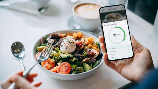 Close up of person using fitness plan mobile app on smartphone with a salad.