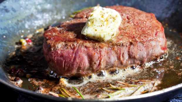 Filet of beef with herb butter, peppercorns, and rosemary frying in a pan.