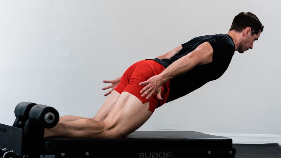 Caucasian man in black T-shirt and red shorts doing Nordic hamstring curl