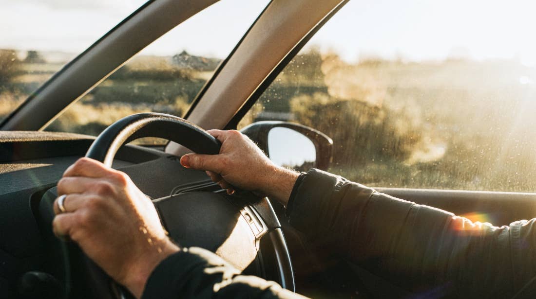 Stock photo of a man's hands on the steering wheel of a car.