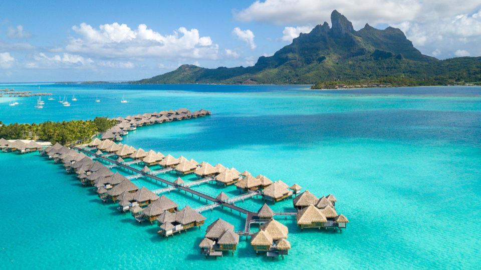Aerial view of overwater bungalows with ocean and mountain background at The St. Regis Bora Bora.