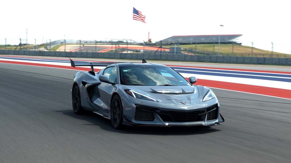 Gray 2025 Chevrolet Corvette ZR1 driving on an F1 track in Texas with American flag in the background, part of new car review.