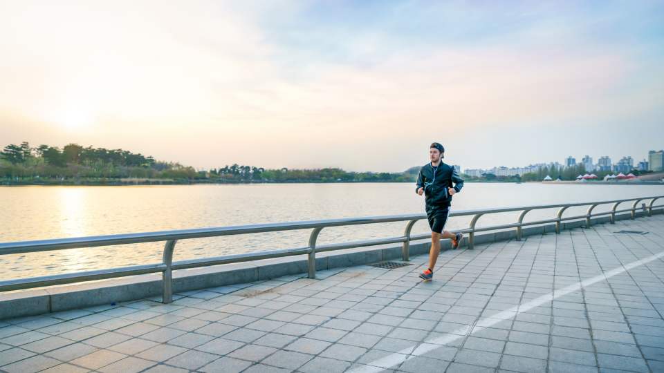 Sporty man with earphones jogging at lake park.