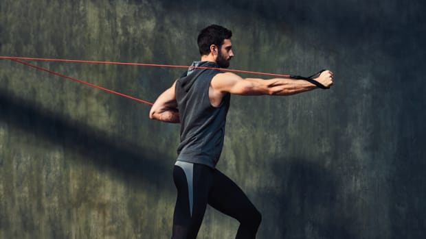 Caucasian man wearing sleeveless hoodie doing cable press