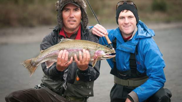 A fly fishing Guide holds a fish that the client caught as they both pose for the camera.
