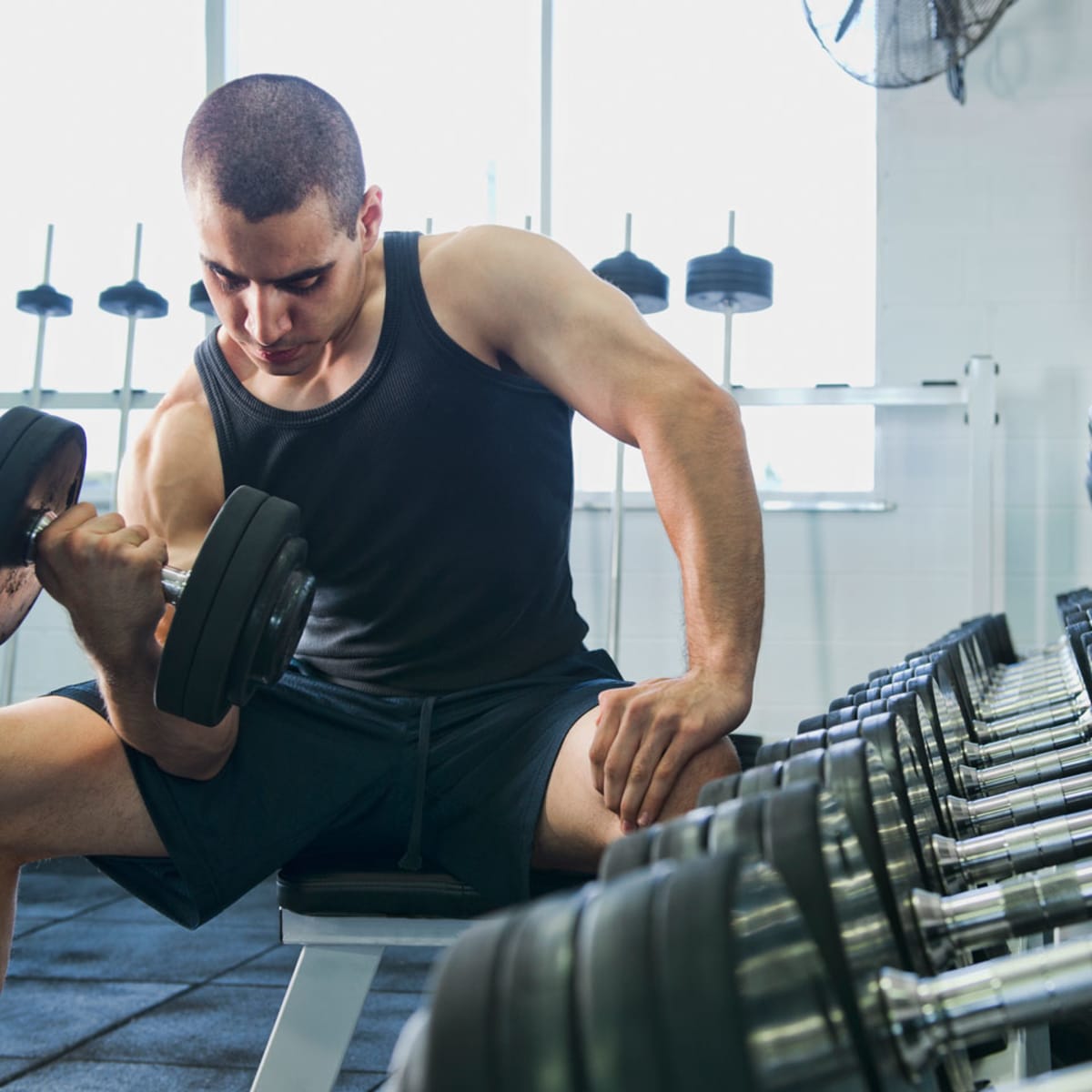 Concentrated man doing dumbbell workout. Well trained body with bulky  muscles. Sport equipment and weightlifting. Stock Photo