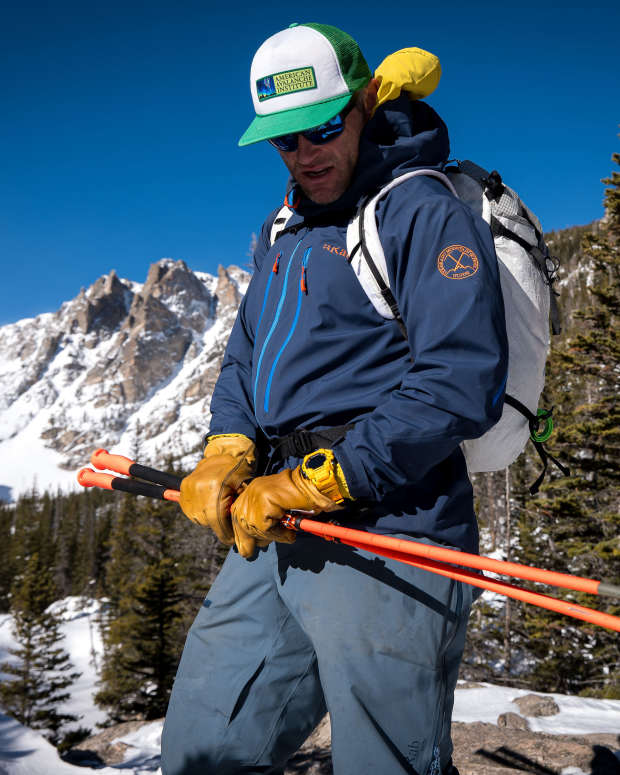 Mountaineer holding ski poles wearing blue ski jacket and yellow G-Shock sport watch with blue sky and mountain range in background