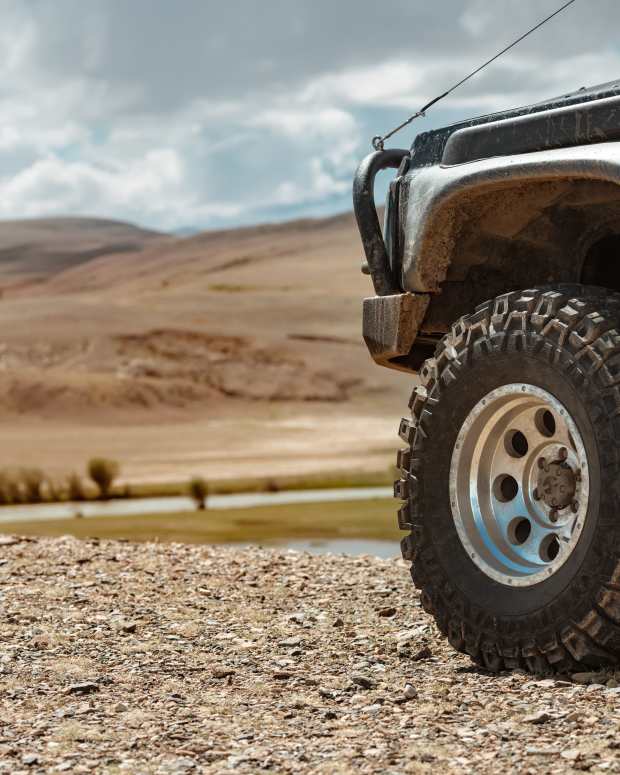Off-road 4x4 truck front end with big wheel and tire with a mountainous desert landscape in the background.