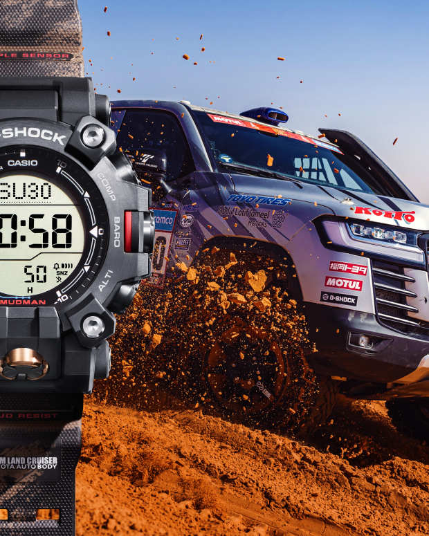 Black and red Casio G-Shock watch superimposed on the left side of an image of a race-ready Land Cruiser driving through sand dunes.