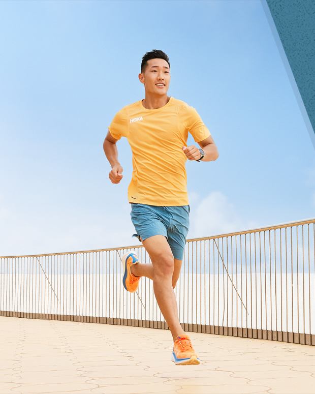 Man running near a beach with orange shirt and teal shorts with a blue sky in the background next to a composite image of two running shoes on a blue background.