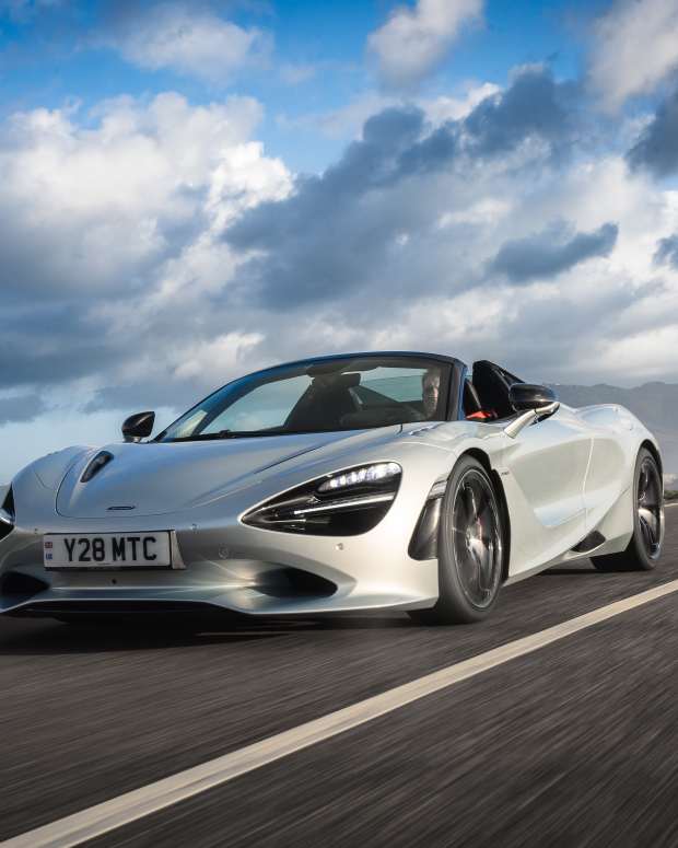 Silver McLaren 750S driving down a road with mountains and clouds in the background that was driven for a first drive car review.