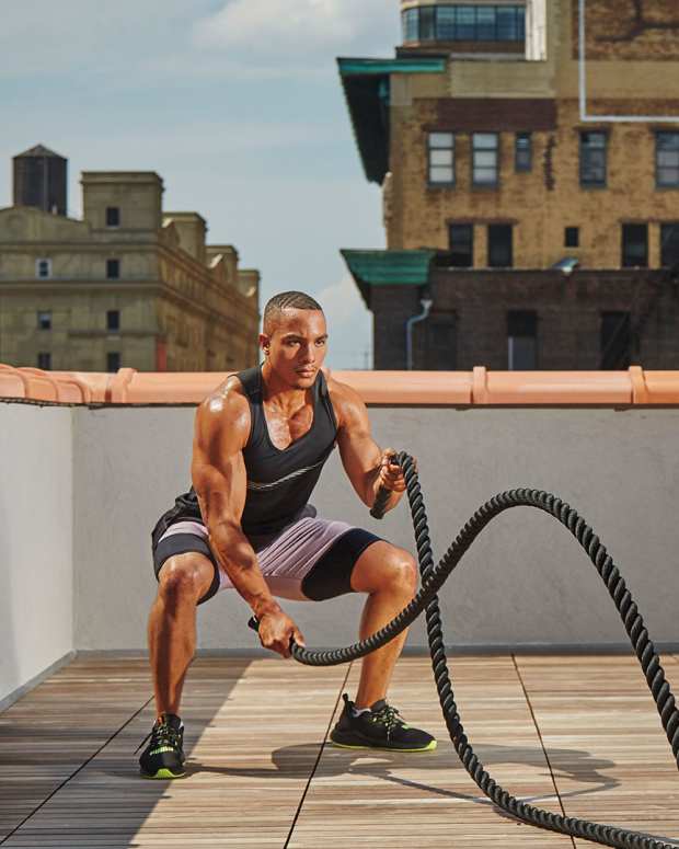Black athletic man on urban rooftop doing battle rope waves, among the best love handle exercises