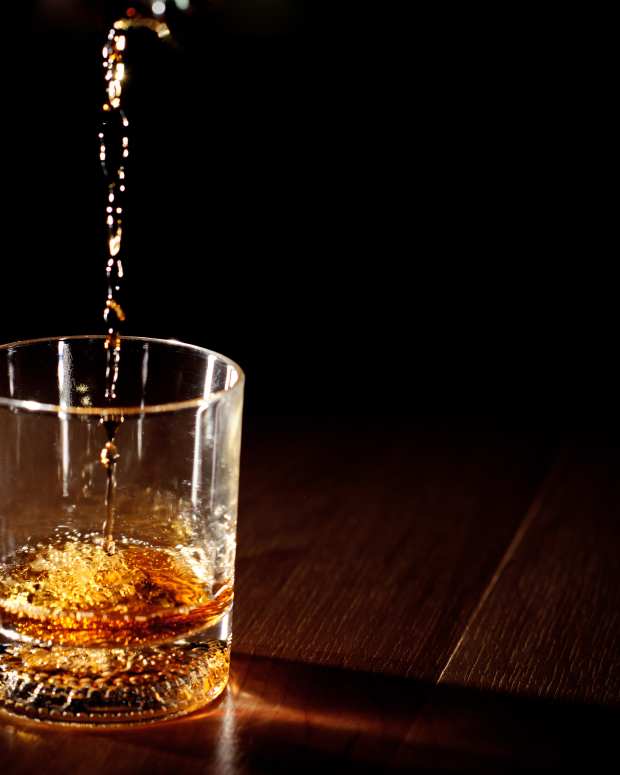 Scotch or bourbon whiskey (or whisky) being poured into a glass with dramatic studio lighting and a black background.