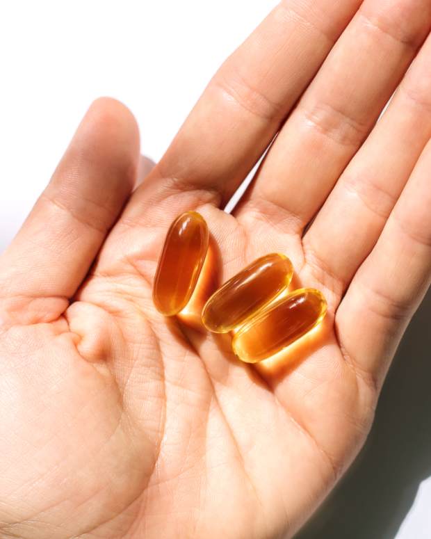 Woman's hand holding fish oil supplements on white background.