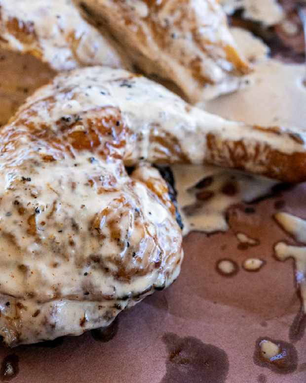Grilled chicken covered in alabama white sauce on butcher paper, part of a Men's Journal article on how to make barbecue sauce.
