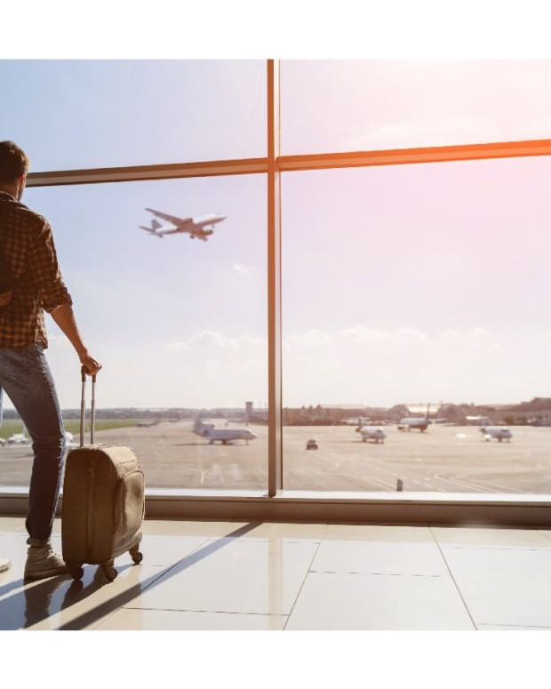 Man with carry-on in airport staring at plane in the air.