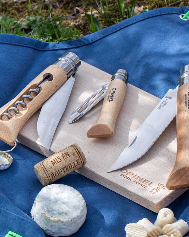 Steel and wood Opinel Nomad Cooking Kit on a blue towel with fruit, cheese and bread on grass, part of Men's Journal Gear of the Week.