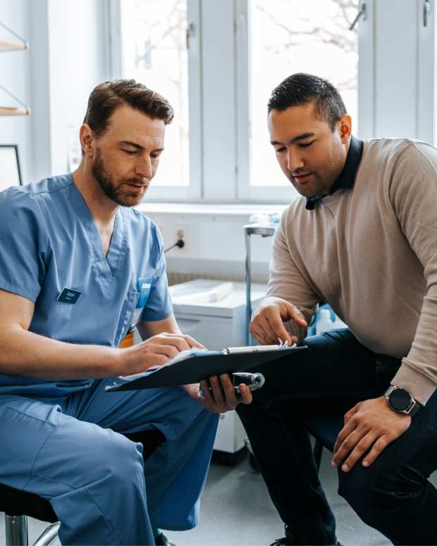 Male medical expert discussing reports with male patient during visit at hospital.