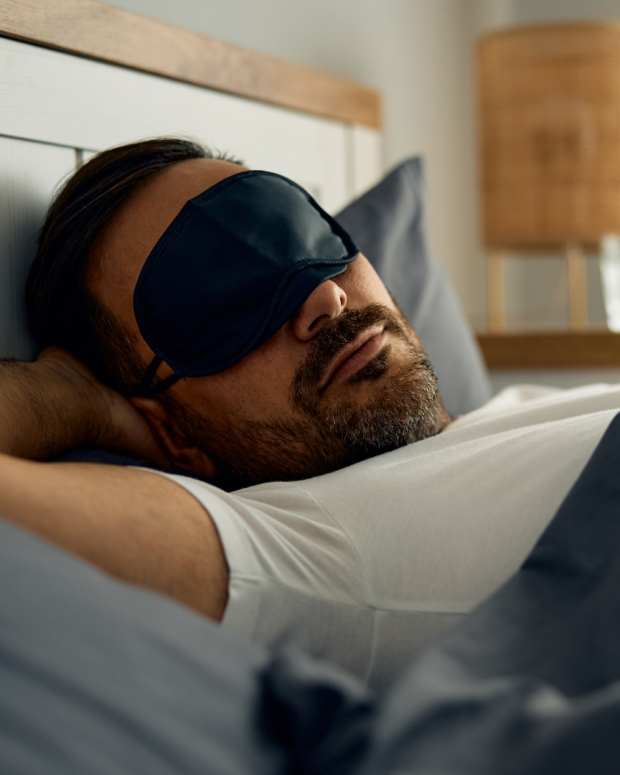 Mid adult man wearing eye mask while sleeping in bed.