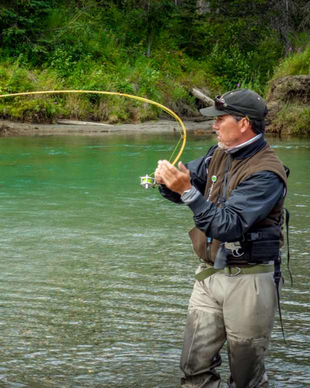 A fly angler has a serious bend to his fly rod while fighting a fish in a clear green river.