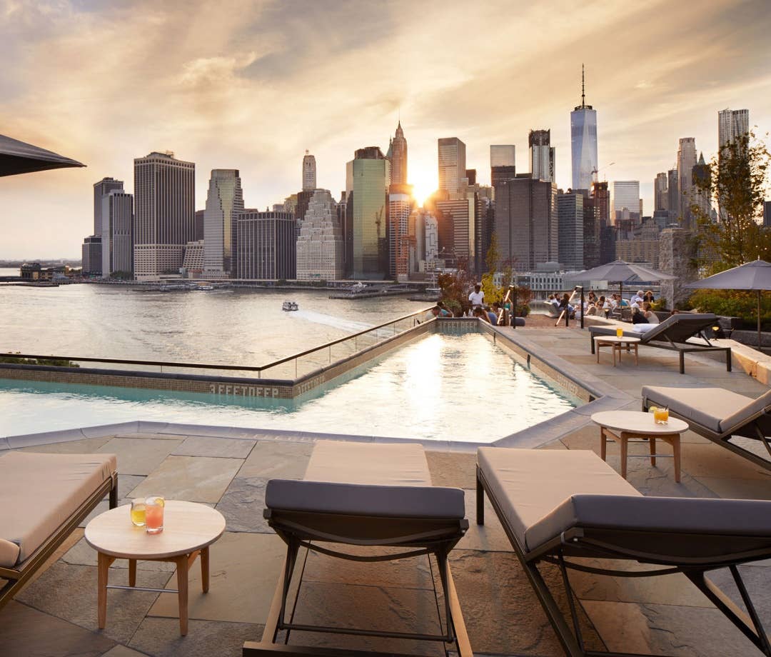 View of the pool at 1 Hotel Brooklyn Bridge at sunset with the Manhattan skyline in the distance. hotel pools