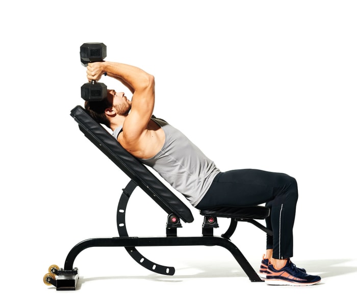 Caucasian man doing incline skull crushers with dumbbells as part of his workout