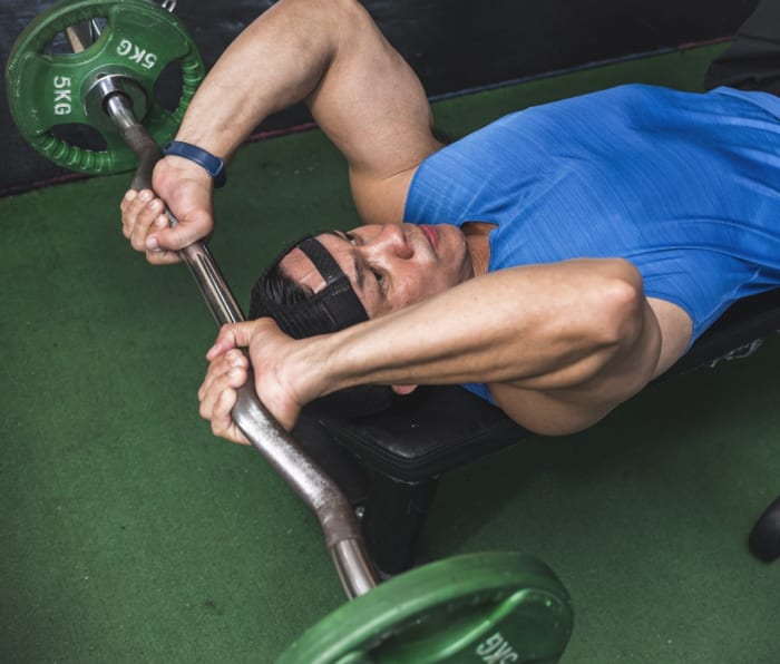 Caucasian man wearing blue tank top doing EZ bar skullcrusher