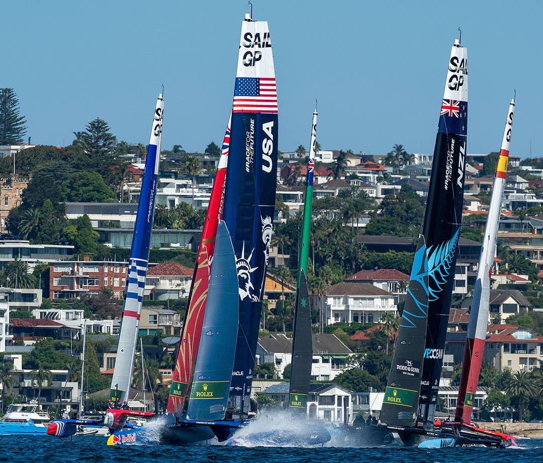 SailGP boats racing, shore background.