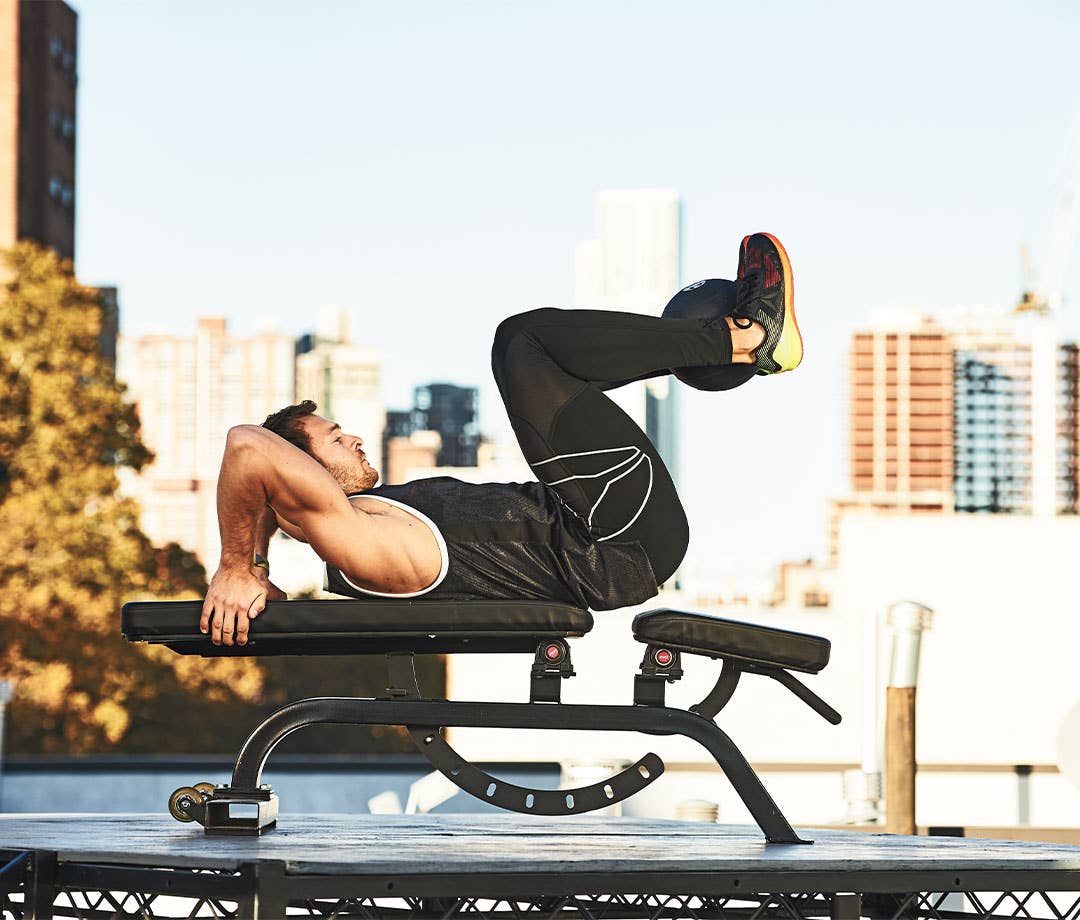 Ab Exercises: Caucasian man in black tank top and black shorts performs knee tuck crunch.