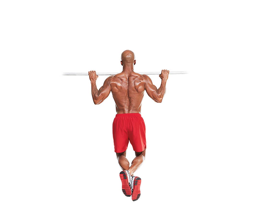 Shirtless black man in red shorts performs pullup.