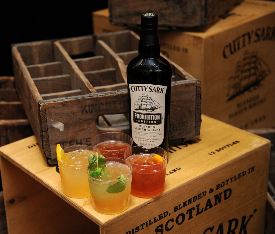 Bottle of Cutty Sark on a box next to cocktails.