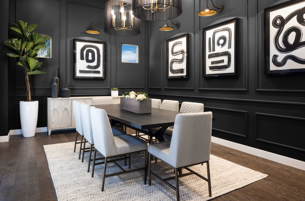 A dining room with a table that seats eight, black walls with trim, and black and white artwork.