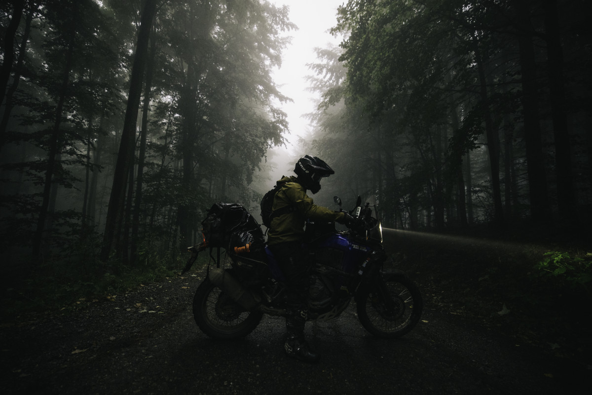 Motorcyclist poses on bike amidst fog on road going through wooded area of Silk Road