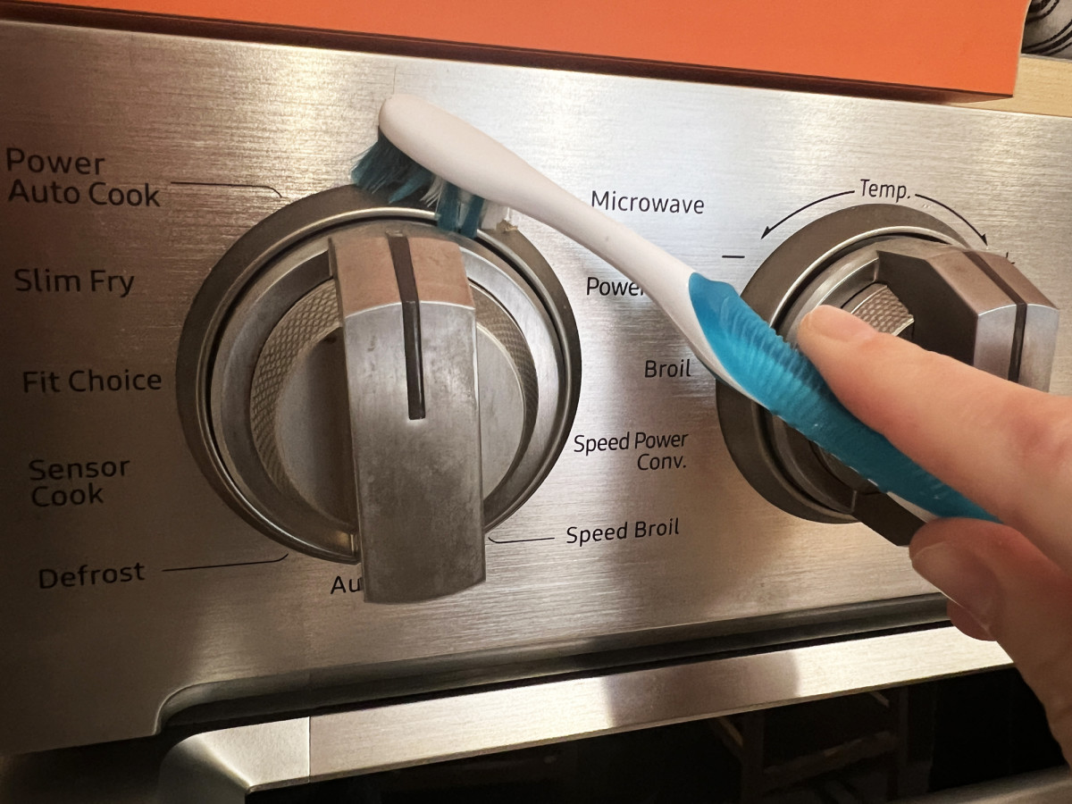 Using a toothbrush to clean crevices on a stainless steel oven.