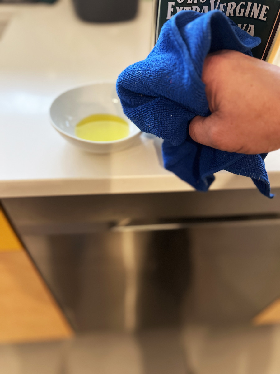 Using olive oil on a microfiber cloth to polish the stainless steel dishwasher.