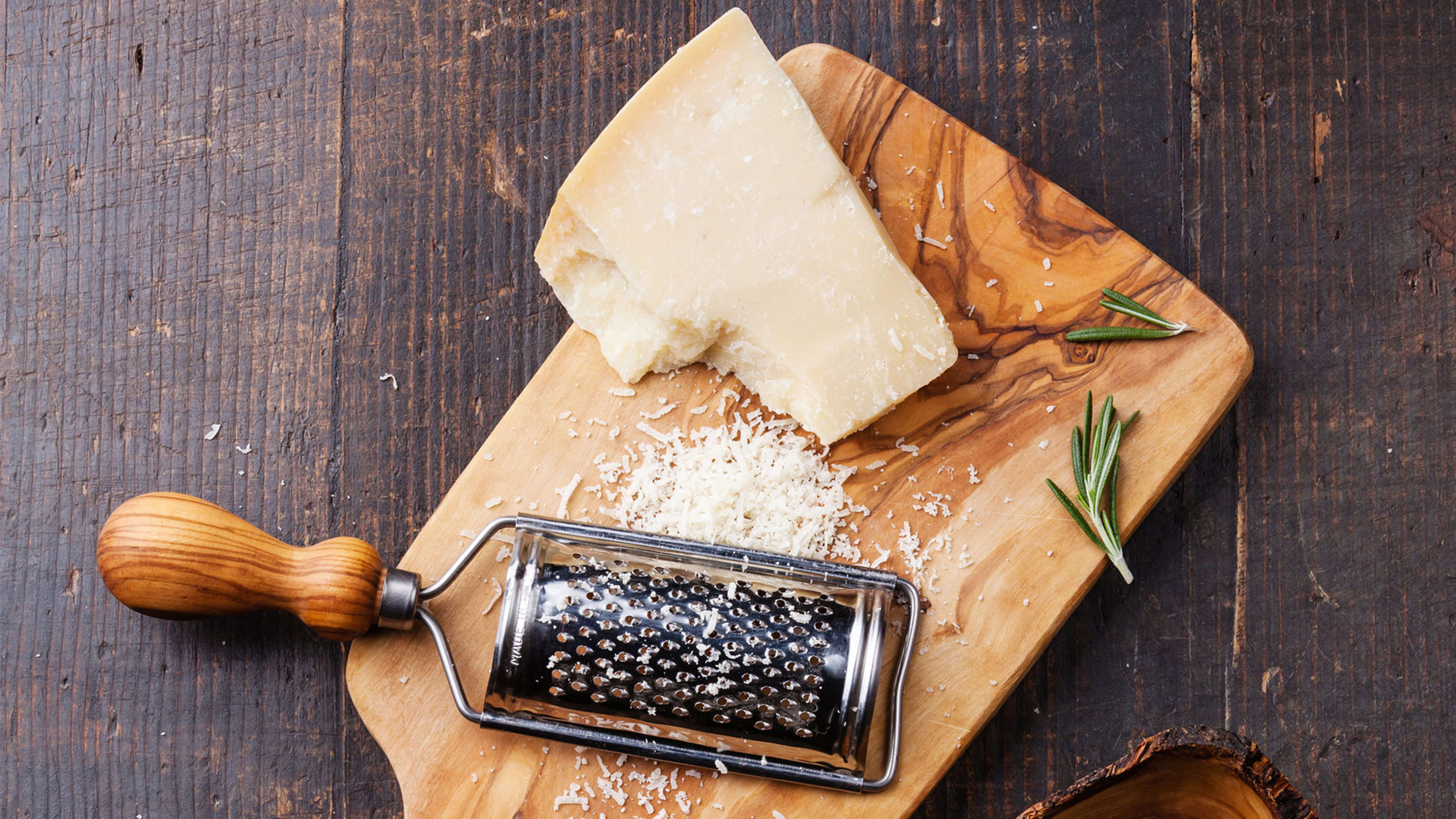 Wedge of Parmesan on olive wood board with rotary grater and rosemary
