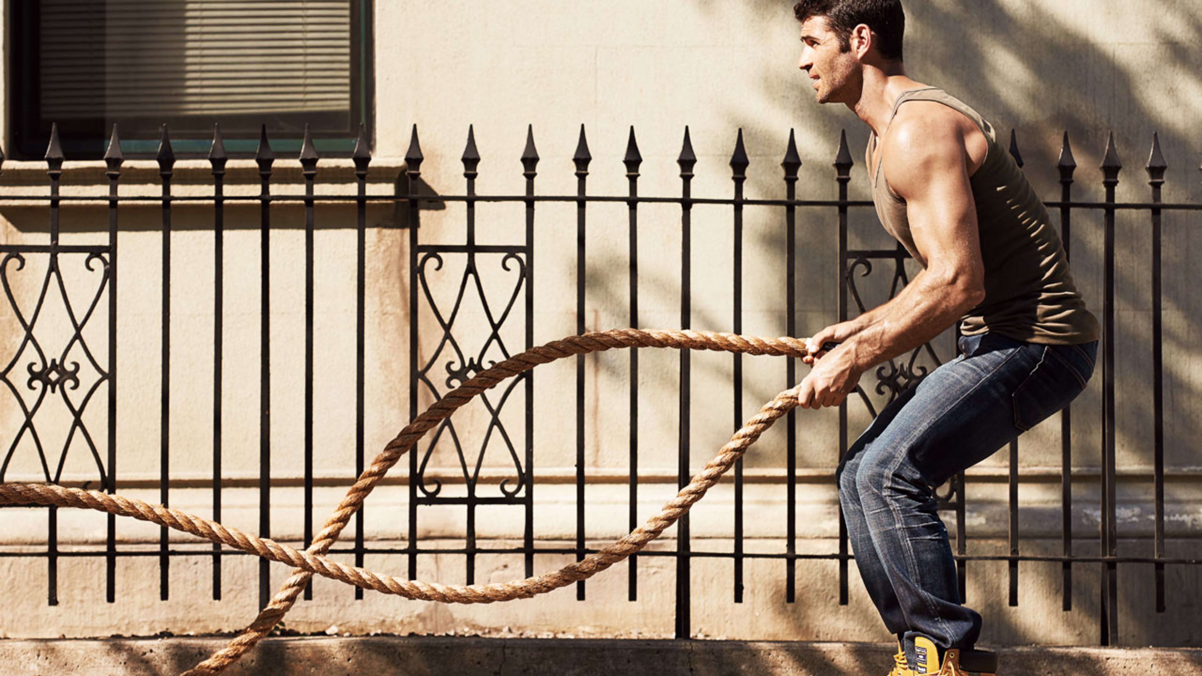 Fit man performing battle rope exercise outdoors, demonstrating high-intensity training