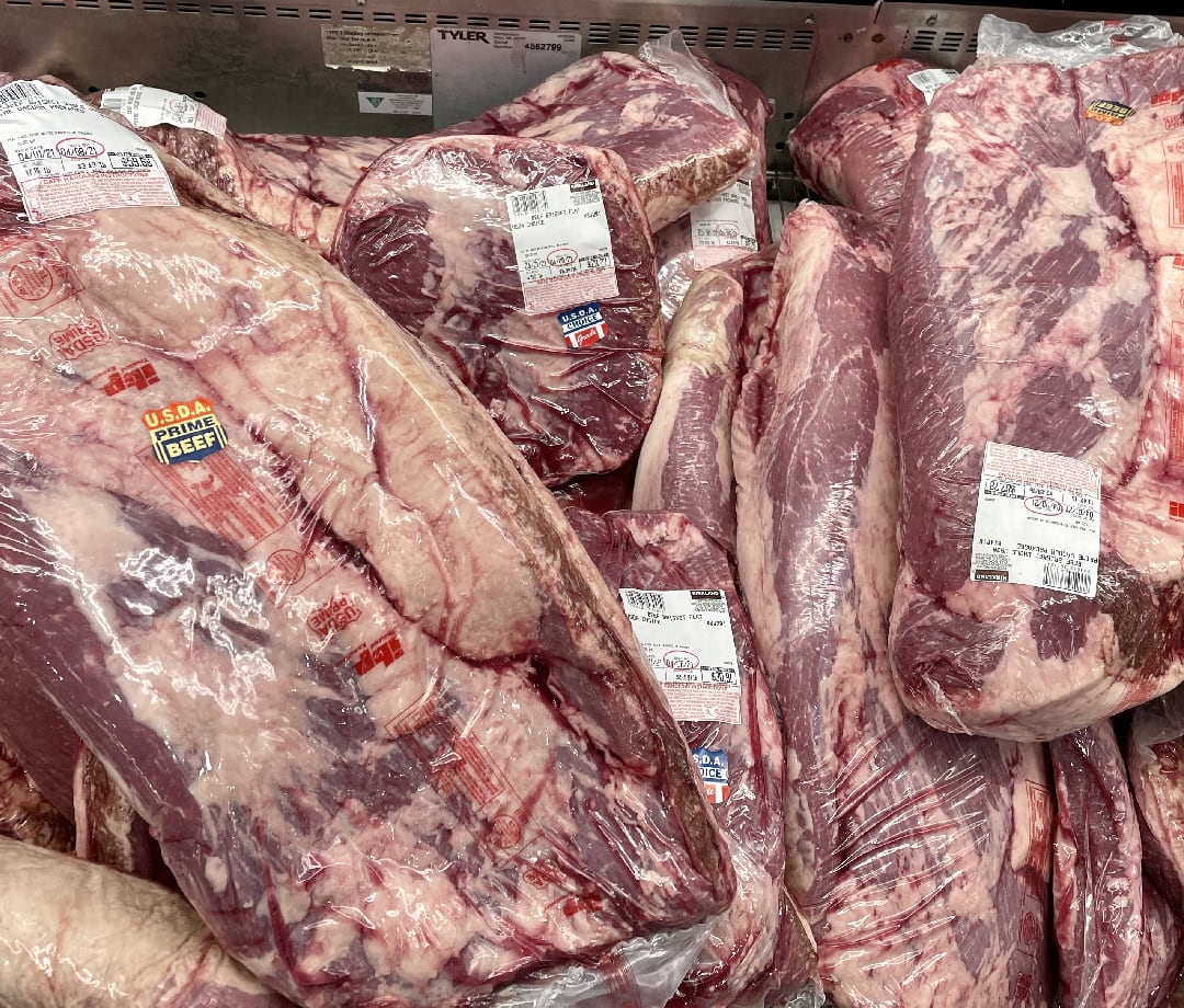 Cryovac packages of brisket in a grocery store cooler.